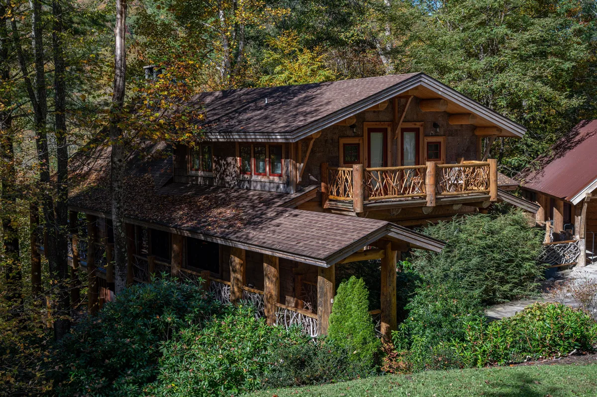 The hero image showcases the stunning exterior of Red Stag Lodge, featuring a grand stone and wood facade, a spacious wooden balcony, and the lush, wooded surroundings of Eagles Nest in Banner Elk. The balcony invites guests to unwind while taking in panoramic sunset views, with the tranquil forest and greenery providing a serene backdrop.