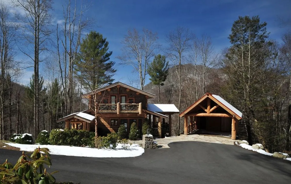 A scenic view of the lodge’s wooden exterior surrounded by mature trees, a stone pathway leading to the entrance, and a garage structure nearby. The image conveys a sense of rustic mountain charm and positions the property as a cozy base camp for outdoor adventures.