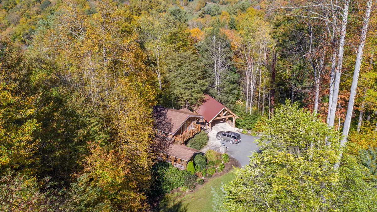 An expansive view of the main lodge structure, highlighting its grand entrance, surrounded by mature trees and a broad driveway. The natural landscape hints at hiking trails and outdoor amenities, while the sense of space and privacy sets the stage for exclusive group experiences.