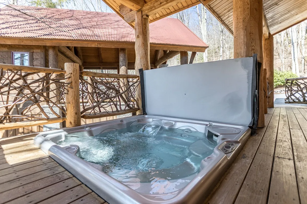 A bubbling hot tub set on a wooden deck, surrounded by lush natural greenery. The intimate and private setting invites guests to soak under the open sky, with the tranquility of the forest enhancing the sense of relaxation and privacy.