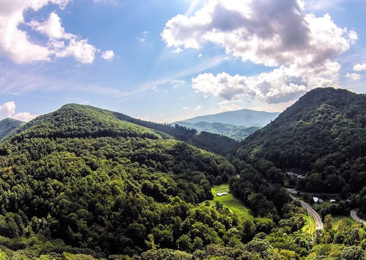 A breathtaking panoramic view of the Blue Ridge mountain ranges, lush greenery, winding roads, and a cloudy sky. The scene evokes the grandeur and beauty of the High Country’s natural landscape, ideal for hiking, biking, and scenic drives.