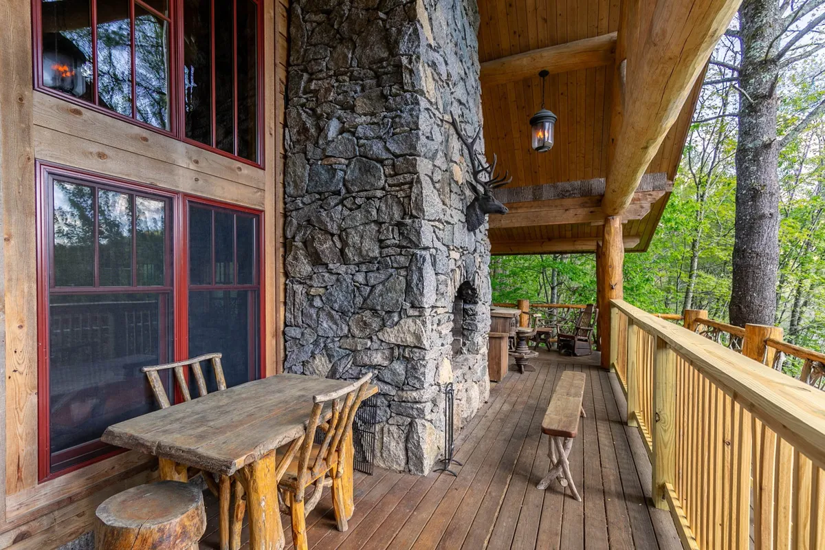 An outdoor dining area with a stone fireplace, wooden table, and surrounding greenery. The space is designed for shared meals, cozy gatherings, and enjoying the outdoors in comfort.