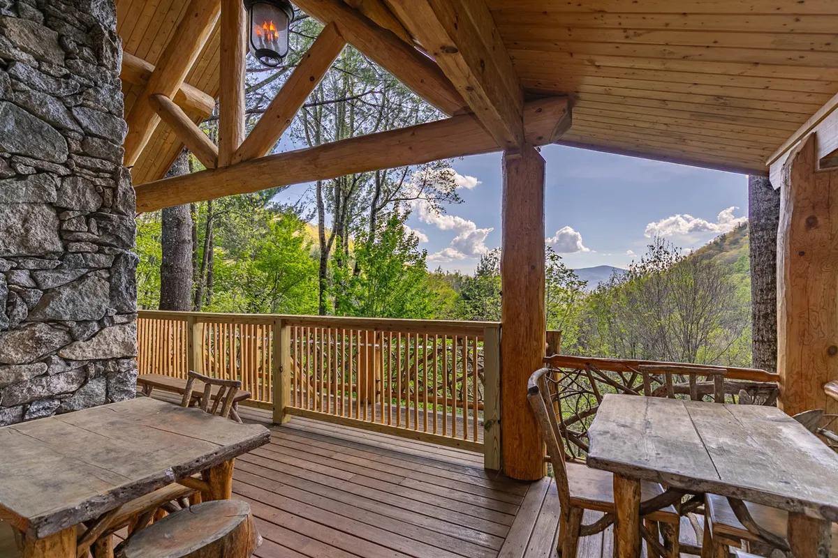 A tranquil wooden deck furnished with rustic outdoor furniture, overlooking a sweeping mountain view. The stone wall provides privacy while still allowing guests to immerse in the natural beauty surrounding the property. The deck is perfectly suited for relaxing, reading, or enjoying an alfresco meal while taking in the peaceful atmosphere.