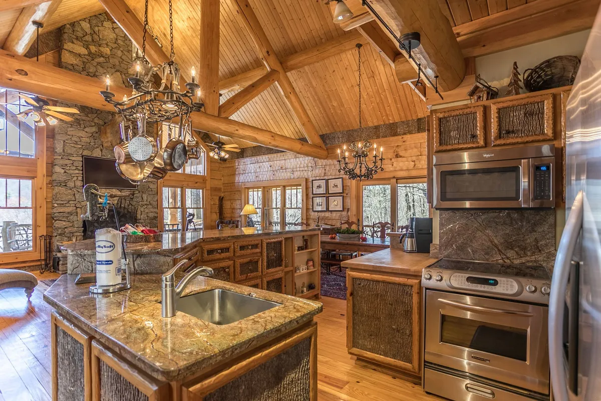The kitchen is highlighted in this photo, featuring a large central island, a beautiful chandelier, stone accents, and oversized windows that flood the space with natural light. The setup is perfect for cooking, entertaining, and gathering, aligning with the gourmet kitchen's role described in the section.